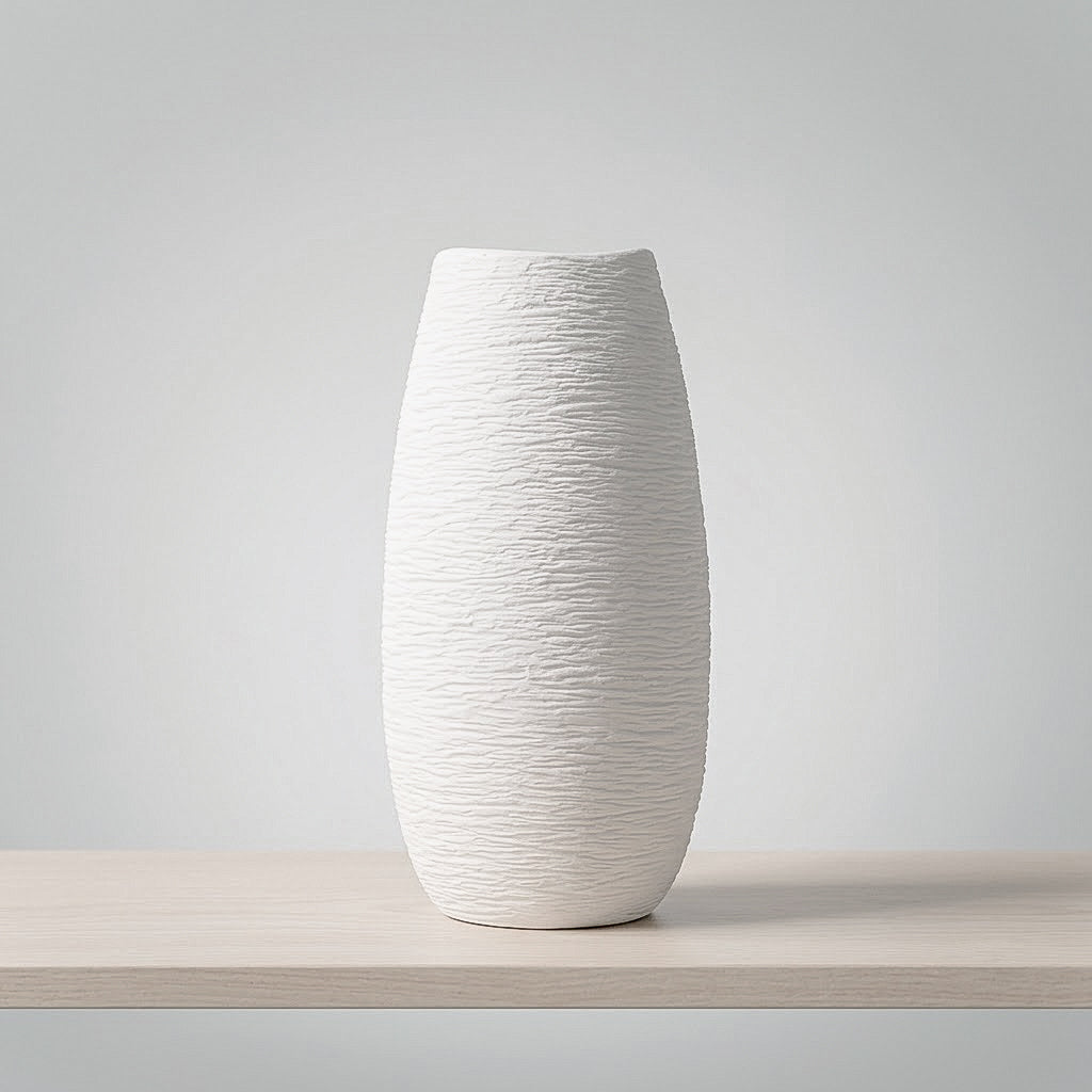 A tall, textured white ceramic vase with a flared rim, displayed on a light wood shelf against a neutral gray background.