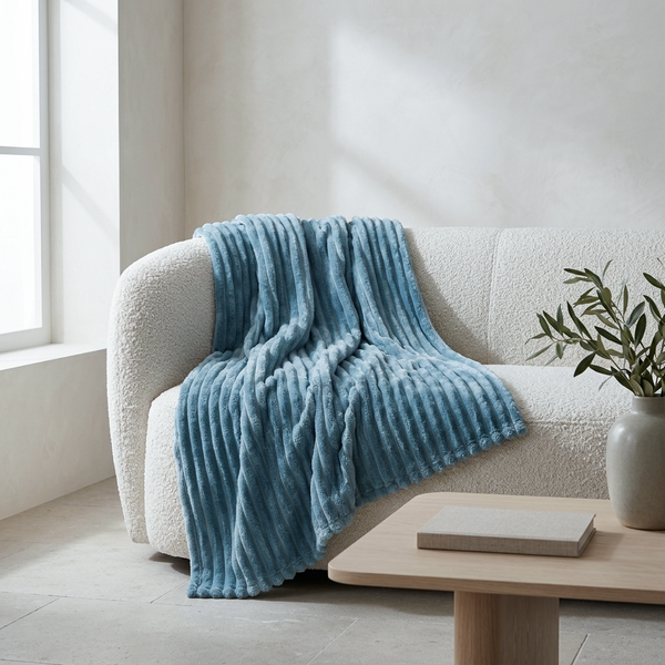 A textured light blue throw blanket with vertical ribbed stripes is draped over a cream boucle sofa in a bright, modern living room setting.
