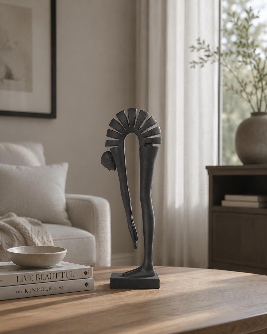 A dark charcoal gray abstract sculpture of two intertwined human figures stands on a wooden coffee table in a modern, softly lit living room.