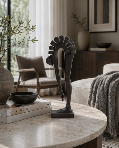 A dark bronze abstract sculpture of a stylized figure on a round marble-top table in a modern, sunlit living room.