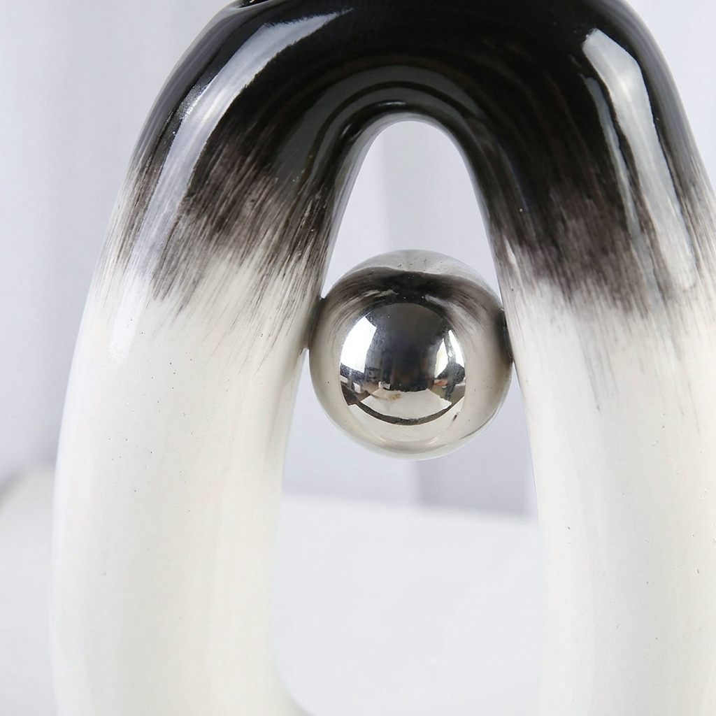 Close-up of a glossy black and white penguin-shaped decorative object with a shiny silver metallic ball at the center, photographed against a light neutral background.