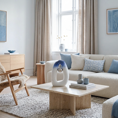 A styled Scandinavian living room interior featuring a cream bouclé sofa with blue accent pillows, a light wood coffee table, a textured rug, and neutral beige curtains in front of a bright window. In the middle is a ceramic vase with blue-white gradient texture.