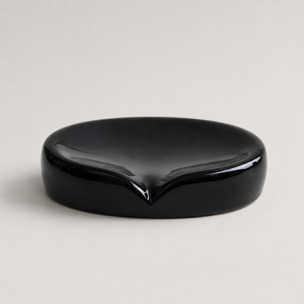 A glossy black ceramic dish with a small pointed depression in the center, photographed on a light gray background.
