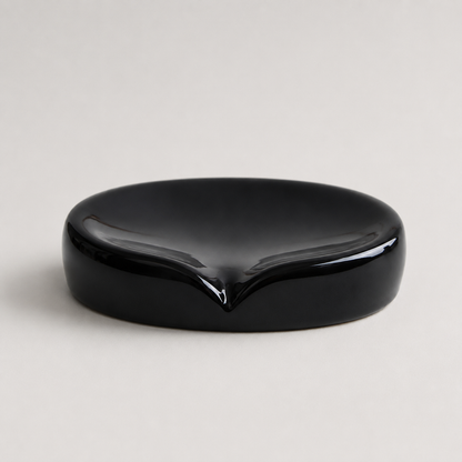A glossy black ceramic dish with a small pointed depression in the center, photographed on a light gray background.