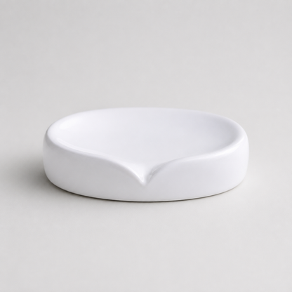 A minimalist white ceramic soap dish with a small pouring spout, photographed on a clean, light gray background.