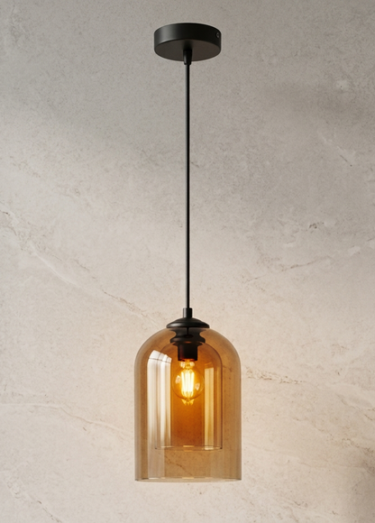 A single pendant light with a black metal canopy and cord, featuring a warm amber-tinted glass shade that glows with the illuminated bulb inside, set against a textured light beige wall.