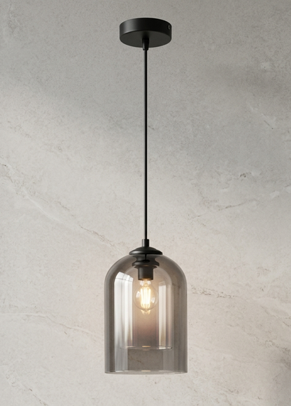 A modern pendant light with a black ceiling canopy and cord, featuring a smoky translucent glass bell shade that reveals a warm glowing Edison bulb, set against a textured light gray wall.