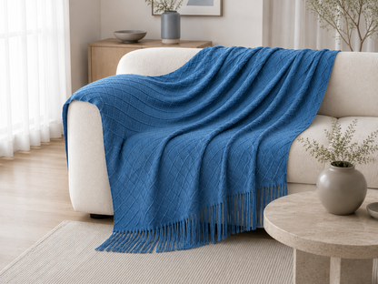 A bright blue textured throw blanket with fringe is draped over a cream-colored sofa in a modern, sunlit living room.