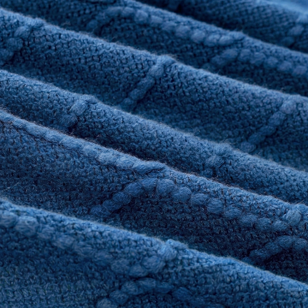 Close-up of a textured blue cable-knit fabric with diagonal ribbed rows and a soft, plush surface.