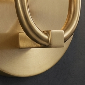 Close-up of a round pull handle with a brushed brass finish and a square decorative wall scone, mounted on a matching round backplate against a dark gray background.