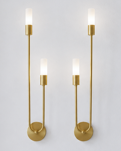 A pair of modern wall-mounted sconces with brushed gold metal arms and cylindrical frosted white glass shades, shown against a light gray wall.