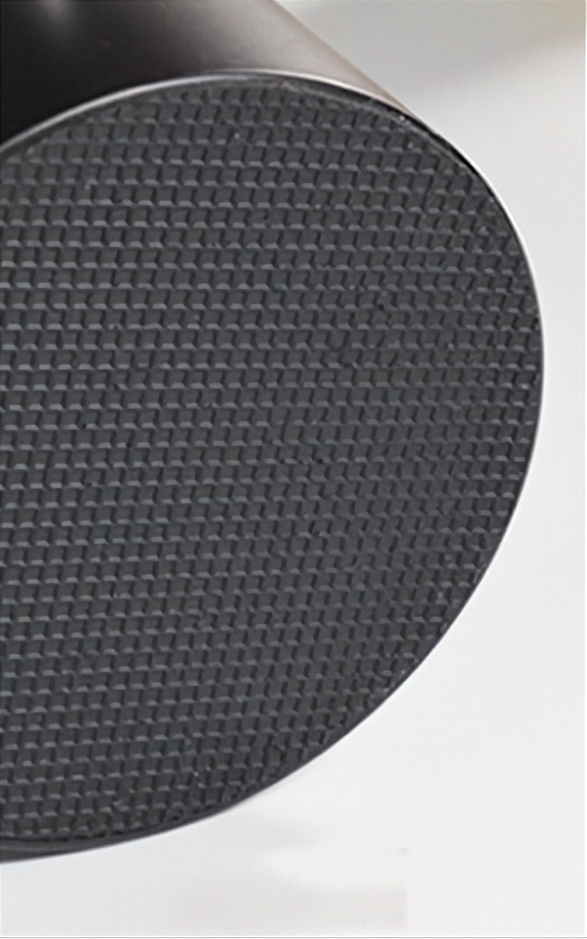 Close-up of a black textured circular disc with a fine woven or grid-like surface, shown against a white background.