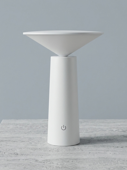 A minimalist white Mushroom table lamp with a wide, shallow conical shade and a cylindrical base featuring a power symbol, set against a solid gray background on a light gray stone surface.
