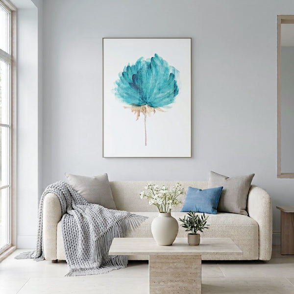 A framed watercolor art print of a teal blue water lily on a white background, hanging on a light gray wall above a modern beige sofa in a bright, contemporary Scandinavian living room.