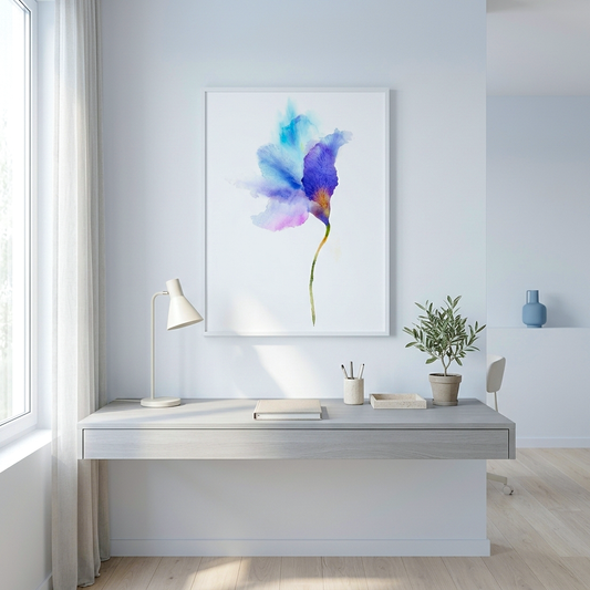 A framed watercolor art print of a blue and purple flower hanging on a light gray wall above a minimalist desk with a lamp and small plant.