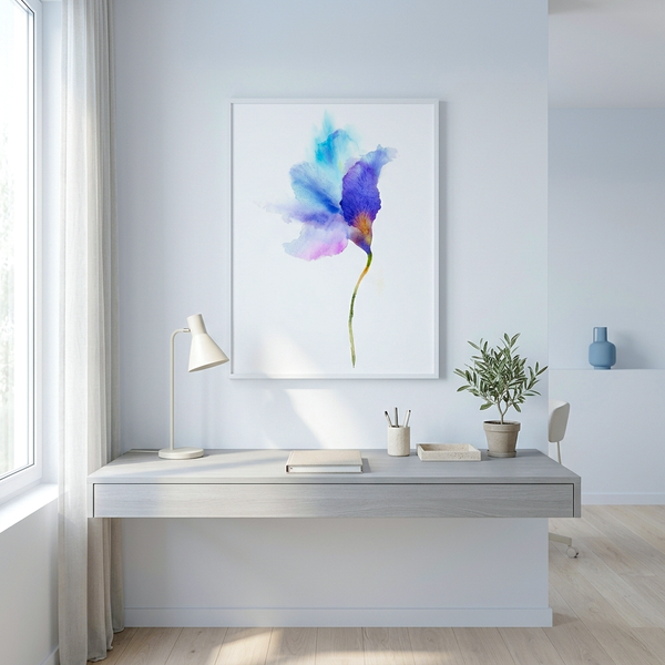 A framed watercolor art print of a blue and purple flower hanging on a light gray wall above a minimalist desk with a lamp and small plant.