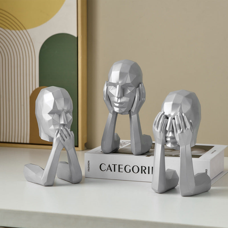 Set of three silver abstract sculpture heads on a white surface with a book titled 'CATEGORI' in the background.