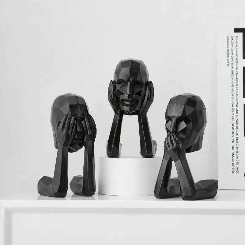 Three black abstract face sculptures on a white surface with a white background