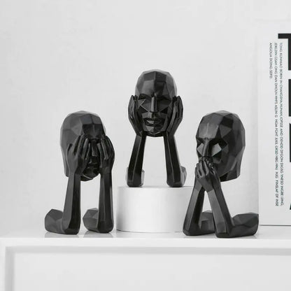 Three black abstract face sculptures on a white surface with a white background