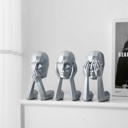Three metallic sculptures of abstract faces on a white surface with a minimal background