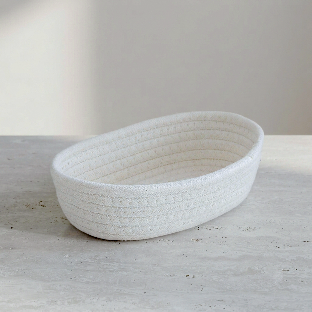 A white woven rope basket with a ribbed texture, photographed on a light gray stone surface against a neutral beige background.