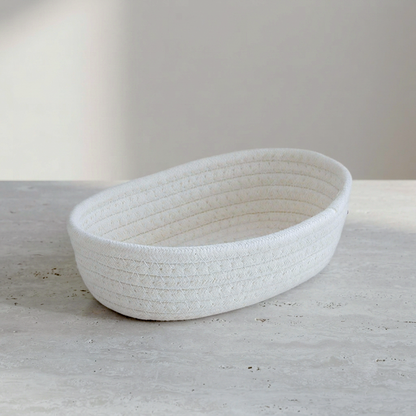 A white woven rope basket with a ribbed texture, photographed on a light gray stone surface against a neutral beige background.