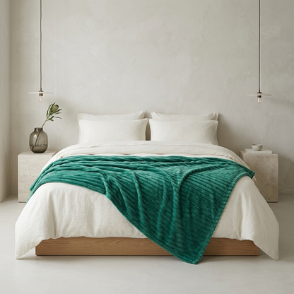 A teal green textured throw blanket draped over a bed with white linens, set in a minimalist modern bedroom with concrete nightstands and pendant lights.